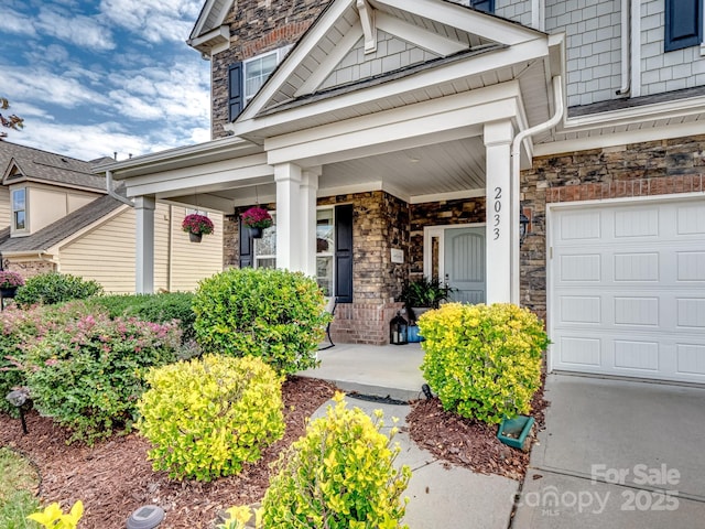 entrance to property featuring stone siding, a porch, and a garage