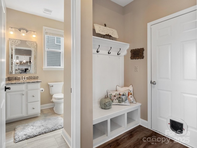 mudroom featuring a sink, visible vents, baseboards, and dark wood finished floors