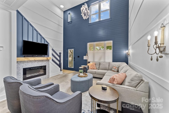 living area with baseboards, a glass covered fireplace, a towering ceiling, wood finished floors, and a notable chandelier