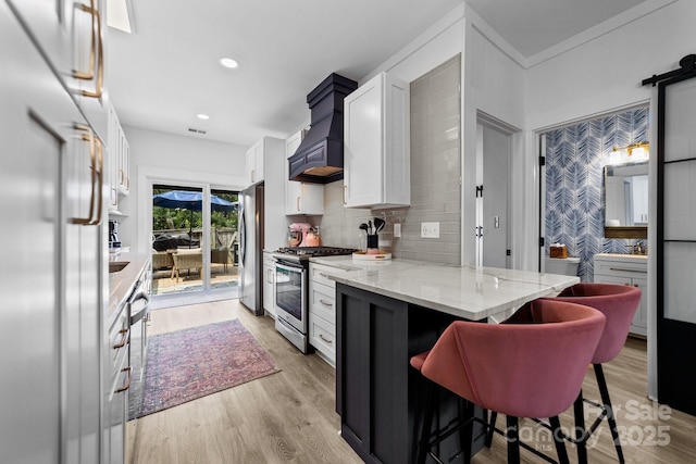 kitchen featuring light wood-style flooring, custom range hood, appliances with stainless steel finishes, and white cabinets