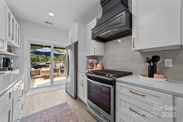 kitchen featuring light wood-style flooring, stainless steel appliances, white cabinets, custom exhaust hood, and decorative backsplash