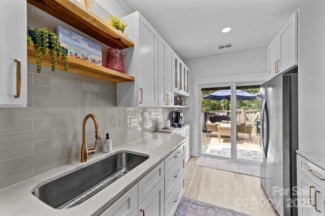 kitchen with a sink, visible vents, freestanding refrigerator, light stone countertops, and open shelves