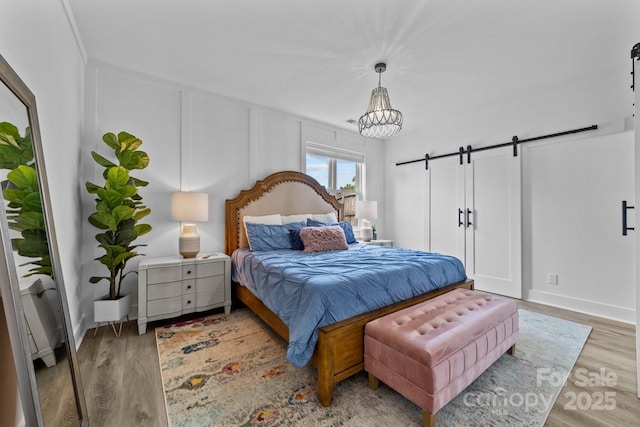 bedroom featuring an inviting chandelier, a barn door, a decorative wall, and wood finished floors