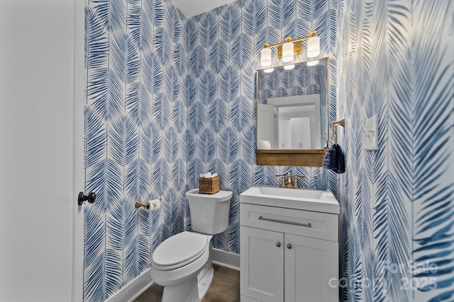 bathroom with toilet, vanity, baseboards, and wallpapered walls