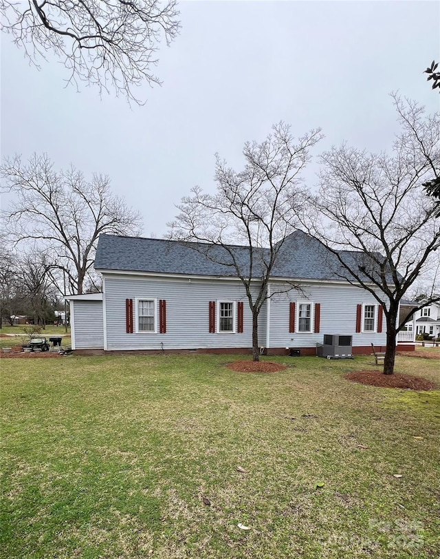 view of front of home featuring roof with shingles, a front yard, and cooling unit