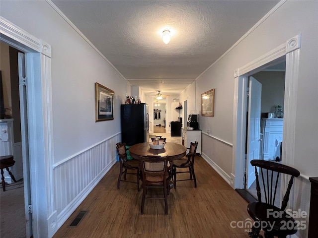 dining area with a textured ceiling, wainscoting, dark wood finished floors, and visible vents