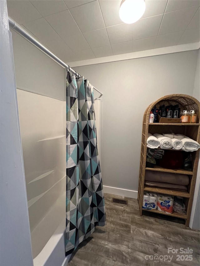 bathroom featuring shower / bath combination with curtain, visible vents, baseboards, and wood finished floors