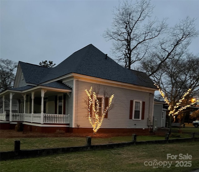 view of side of property with a shingled roof, a porch, and a lawn