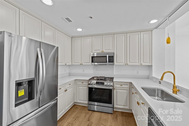 kitchen featuring light wood-style flooring, appliances with stainless steel finishes, light countertops, and a sink