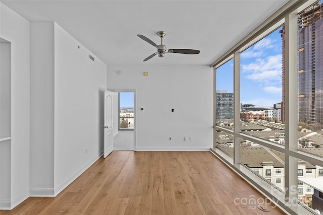 spare room featuring light wood-style floors, expansive windows, a city view, and baseboards