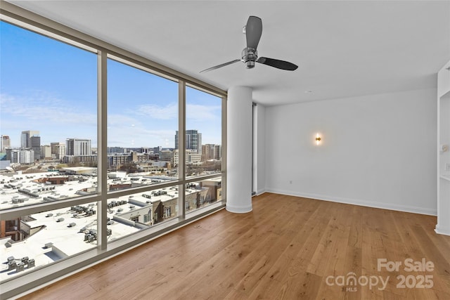 interior space with baseboards, a ceiling fan, wood finished floors, a view of city, and floor to ceiling windows