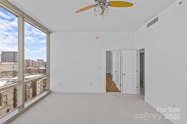 spare room with a city view, visible vents, baseboards, expansive windows, and carpet