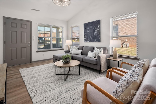 living room featuring vaulted ceiling, wood finished floors, visible vents, and baseboards