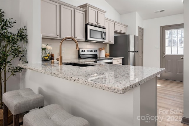 kitchen featuring light stone counters, stainless steel appliances, visible vents, a sink, and a peninsula