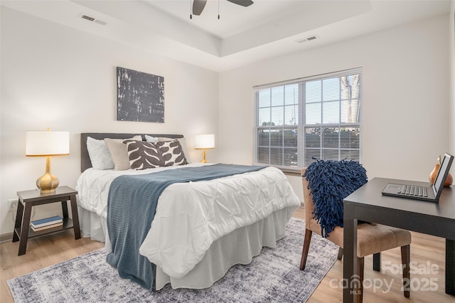 bedroom with light wood-style floors, a tray ceiling, visible vents, and a ceiling fan