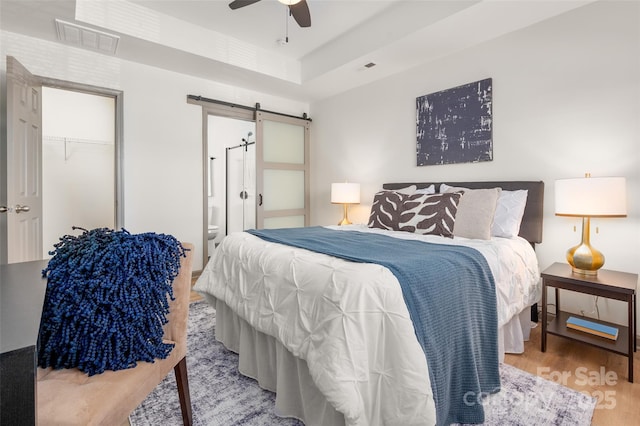 bedroom with a barn door, visible vents, a raised ceiling, a ceiling fan, and wood finished floors