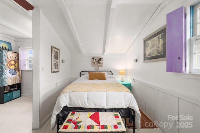 bedroom featuring light wood-style floors, a wainscoted wall, and vaulted ceiling with beams