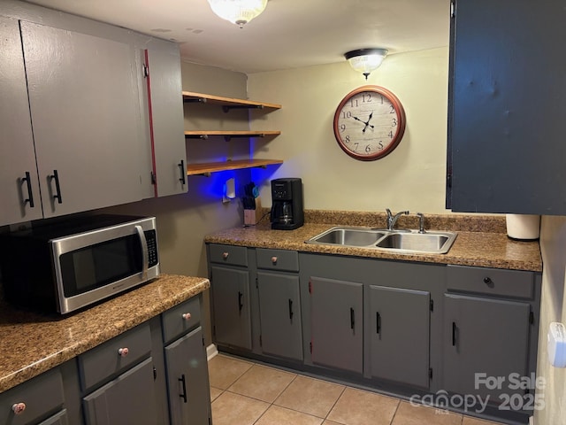 kitchen with light tile patterned floors, gray cabinets, stainless steel microwave, and a sink