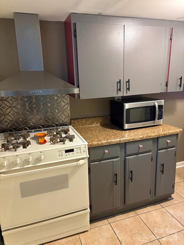 kitchen featuring wall chimney exhaust hood, stainless steel microwave, white gas range, and gray cabinets