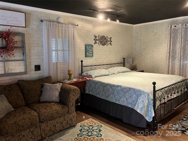 bedroom featuring brick wall, ornamental molding, and wood finished floors