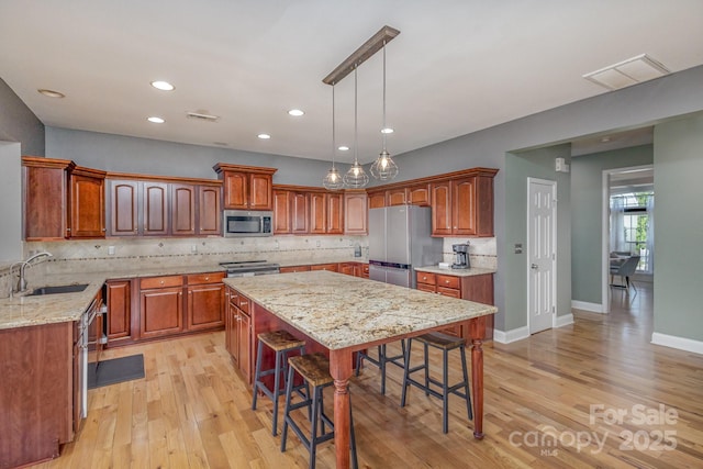 kitchen with visible vents, appliances with stainless steel finishes, a breakfast bar, a center island, and a sink