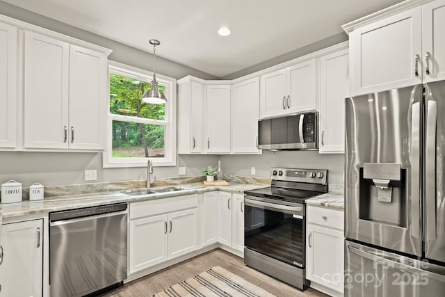 kitchen with light wood finished floors, white cabinets, light stone counters, stainless steel appliances, and a sink