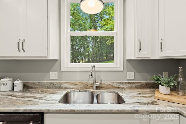 kitchen with light stone counters, white cabinetry, a sink, and dishwashing machine