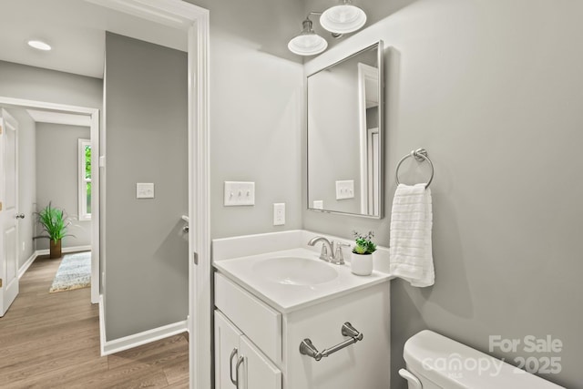 half bathroom featuring vanity, wood finished floors, toilet, and baseboards