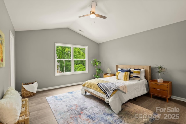 bedroom featuring ceiling fan, wood finished floors, visible vents, baseboards, and vaulted ceiling