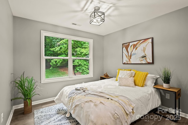 bedroom with baseboards, visible vents, and wood finished floors