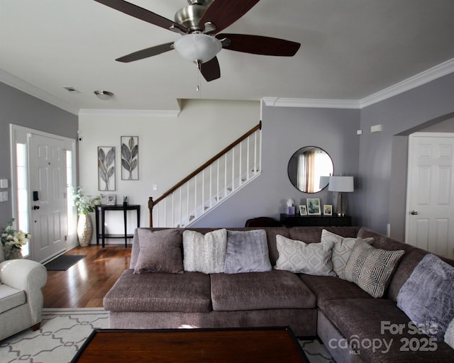 living room featuring crown molding, visible vents, ceiling fan, wood finished floors, and stairs