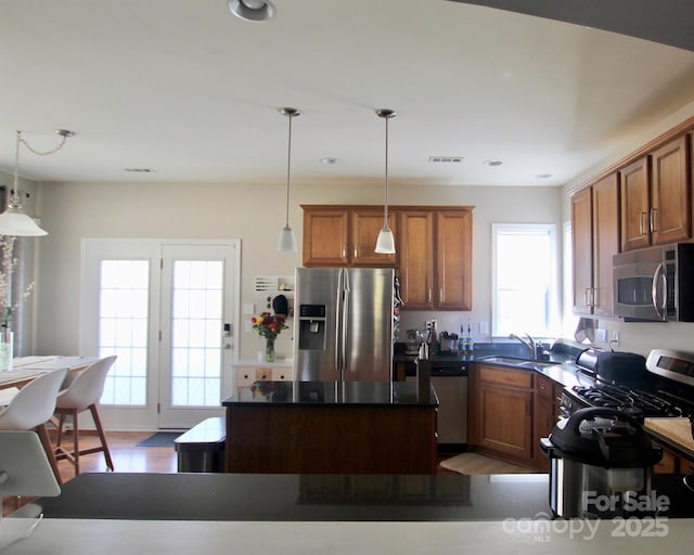 kitchen with brown cabinetry, dark countertops, a center island, stainless steel appliances, and a sink