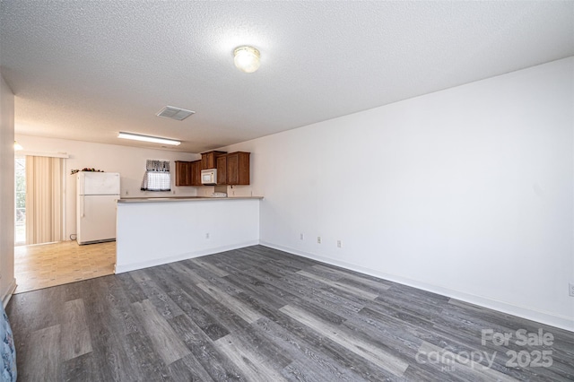 unfurnished living room with visible vents, a textured ceiling, dark wood-type flooring, and baseboards