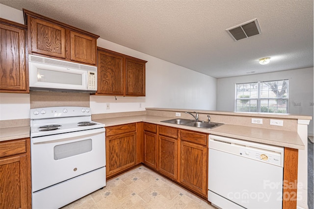 kitchen featuring visible vents, brown cabinets, a sink, white appliances, and a peninsula