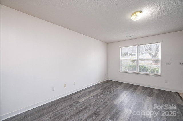 spare room featuring dark wood-type flooring, visible vents, baseboards, and a textured ceiling