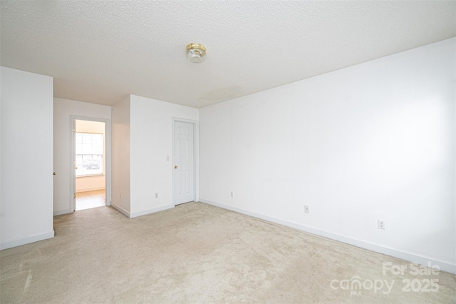 spare room featuring light colored carpet, baseboards, and a textured ceiling