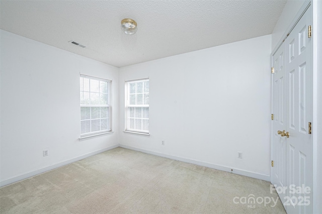 empty room featuring visible vents, light colored carpet, a textured ceiling, and baseboards