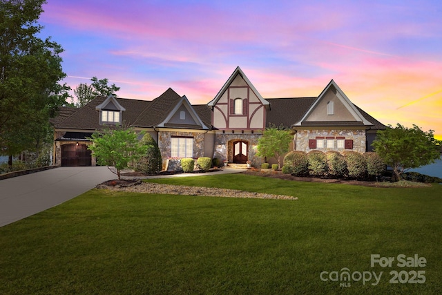 tudor-style house featuring stucco siding, stone siding, a lawn, and driveway