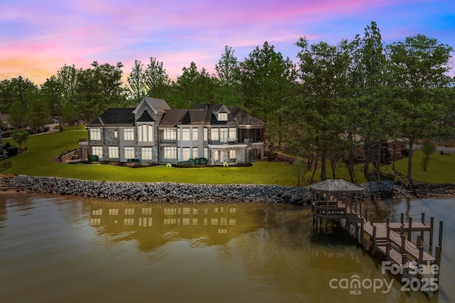 back of property at dusk featuring a water view, a yard, and boat lift