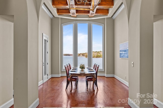 dining room featuring a water view, baseboards, arched walkways, and coffered ceiling