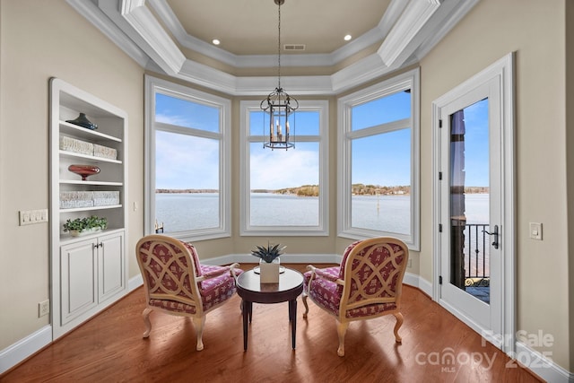 sitting room featuring built in shelves, crown molding, visible vents, a water view, and wood finished floors