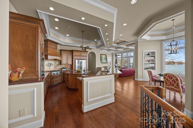 kitchen with stainless steel appliances, ornamental molding, dark countertops, and a center island with sink