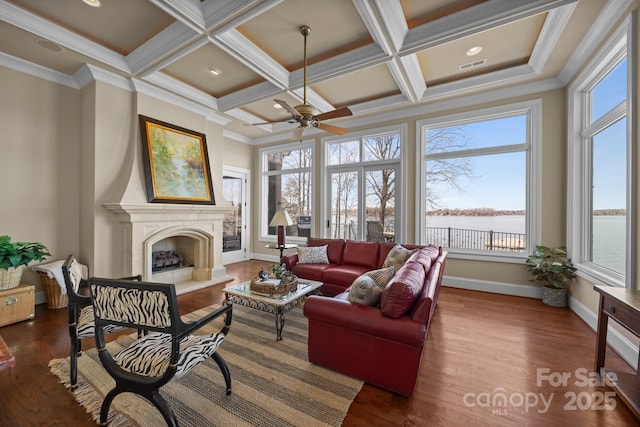 living room featuring a fireplace with raised hearth, ornamental molding, wood finished floors, and baseboards