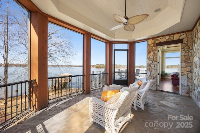 sunroom / solarium with a ceiling fan, a tray ceiling, and a water view