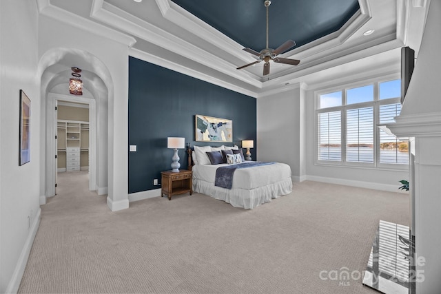 bedroom featuring arched walkways, a tray ceiling, ornamental molding, and baseboards