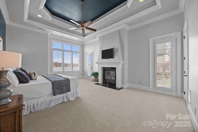 carpeted bedroom with crown molding, a raised ceiling, multiple windows, and a fireplace