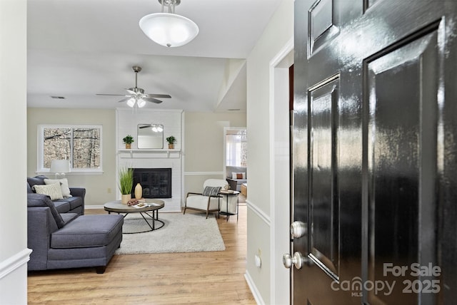 foyer featuring visible vents, light wood-style flooring, a brick fireplace, ceiling fan, and baseboards