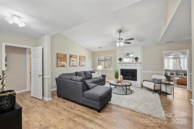 living room featuring light wood finished floors, baseboards, lofted ceiling, ceiling fan, and a brick fireplace