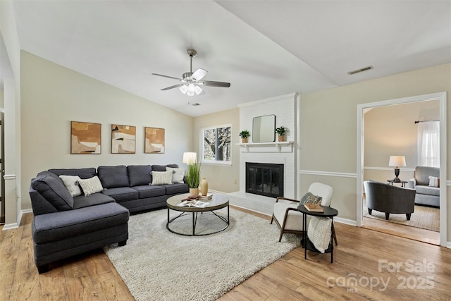 living room featuring vaulted ceiling, a brick fireplace, wood finished floors, and visible vents