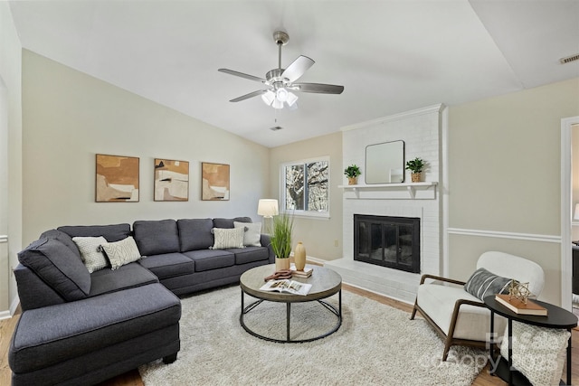 living area with lofted ceiling, visible vents, a ceiling fan, a brick fireplace, and wood finished floors